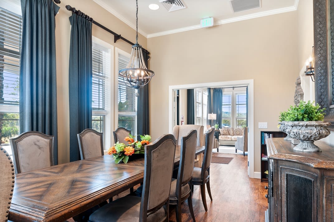 A well-furnished dining room with a large table, chairs, chandelier, and decorative flowers.