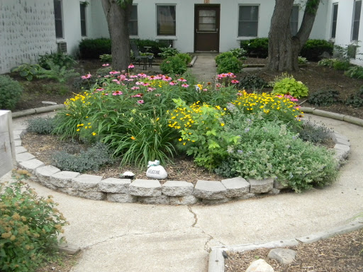 A vibrant garden filled with colorful flowers and lush greenery, surrounded by a stone border and a walking path.