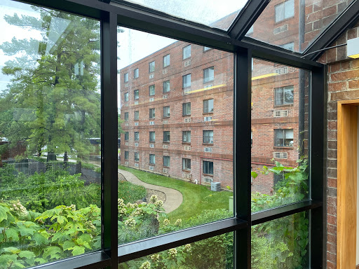 A view through a glass window showcasing a brick building and lush greenery.