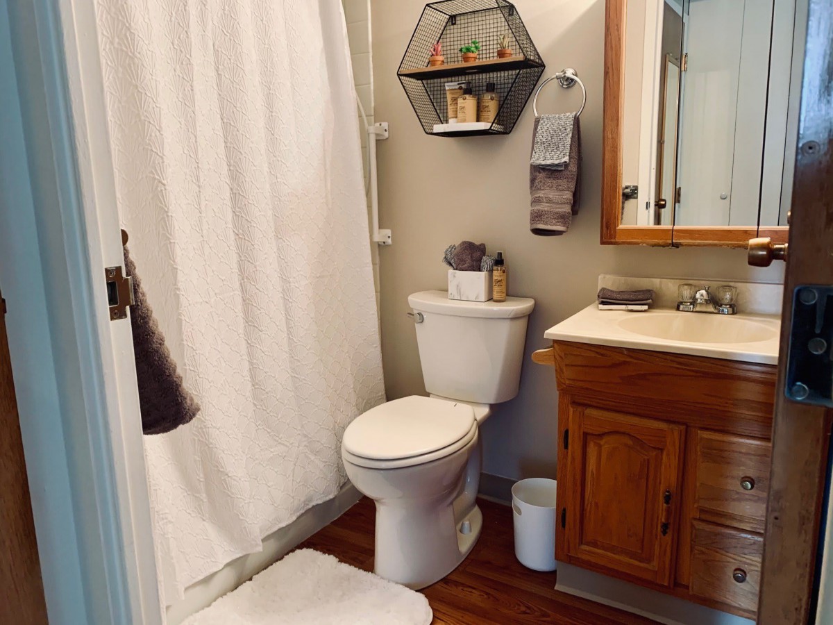A cozy bathroom with a wooden vanity, toilet, and a shower area with a white curtain.