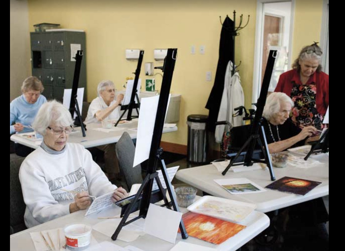 A group of seniors engaged in a painting class, working on their art pieces at easels.