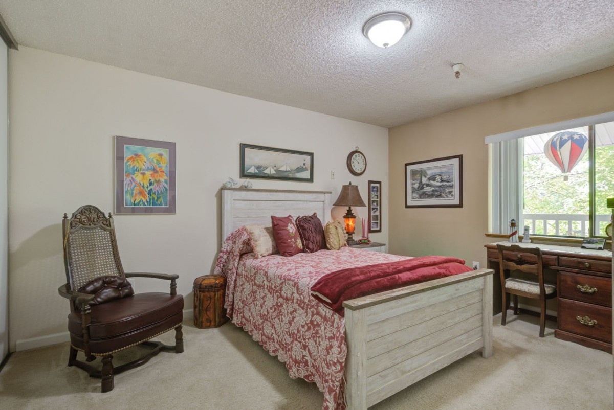 A cozy bedroom featuring a neatly made bed with patterned bedding, flanked by decorative paintings and a bedside lamp.