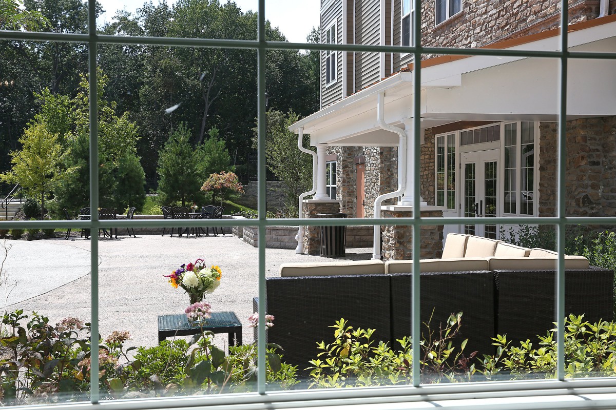 View through a window overlooking a patio with outdoor seating and flowers.