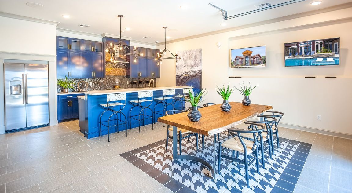 A modern kitchen and dining area featuring blue cabinets, a wooden table, and stylish pendant lights.