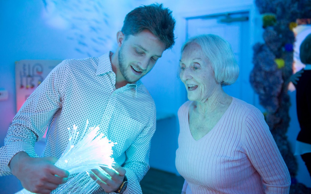 A man and an older woman enjoying a fiber optic light display indoors.