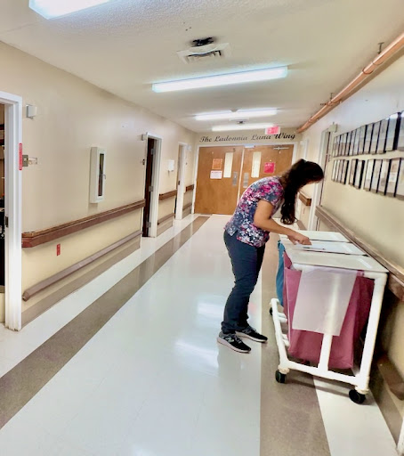 A healthcare staff member organizing or retrieving items from a cart in a hospital hallway.
