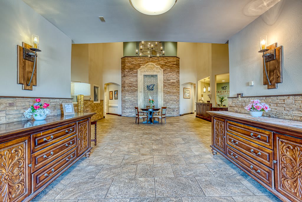 A spacious and elegant foyer with tile flooring, wooden furniture, and a chandelier.