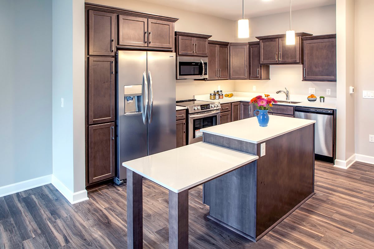 A modern kitchen with wooden cabinets, a stainless steel refrigerator, and an island with pendant lighting.