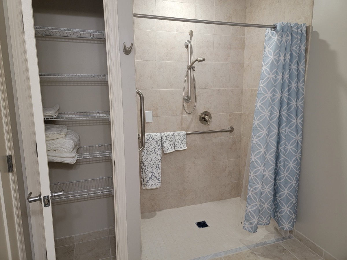 A bathroom with an open shower area, featuring a blue patterned shower curtain and grab bars. Towels are neatly arranged on nearby shelves.