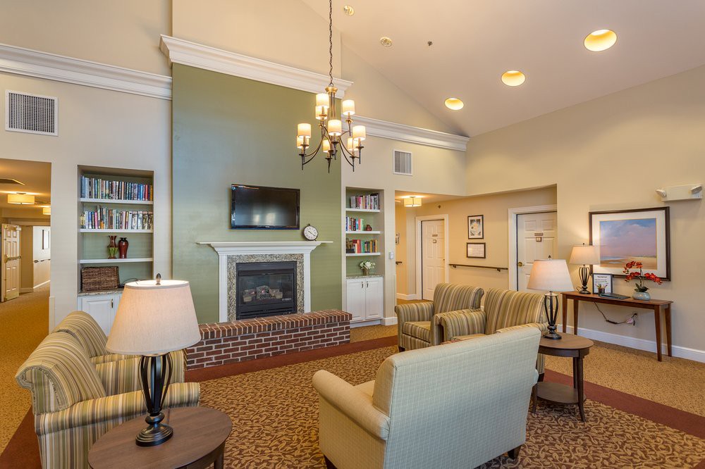 A cozy living room with a fireplace and comfortable seating, illuminated by a chandelier.