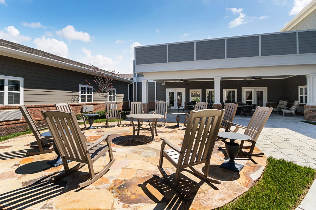 A sunny outdoor patio with rocking chairs arranged around a circular stone seating area.