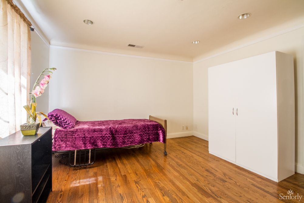 A minimalist bedroom with a single bed covered in purple bedding and a wooden floor.