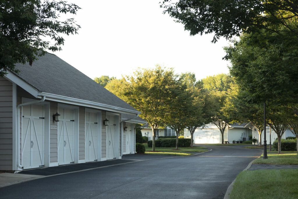 A quiet residential driveway lined with garages and trees basking in sunlight.