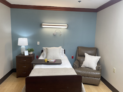 A cozy patient room featuring a comfortable bed, recliner, and soft lighting.