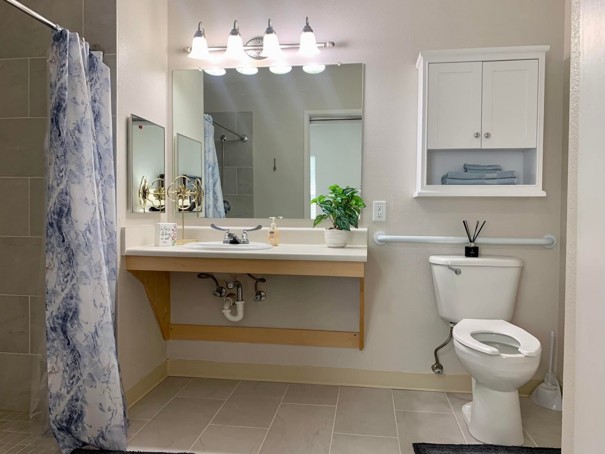 A modern bathroom with a large mirror, sink, toilet, and shower area.