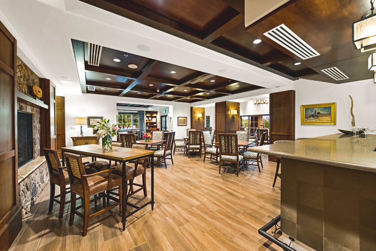A spacious and well-lit dining area with wooden flooring, featuring multiple tables and chairs arranged neatly.