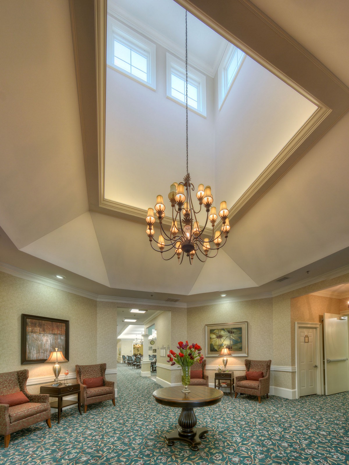 A spacious lobby with a grand chandelier and comfortable seating area beneath a skylight.
