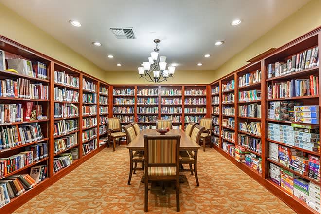 A cozy library reading room with bookshelves and a central table surrounded by chairs.