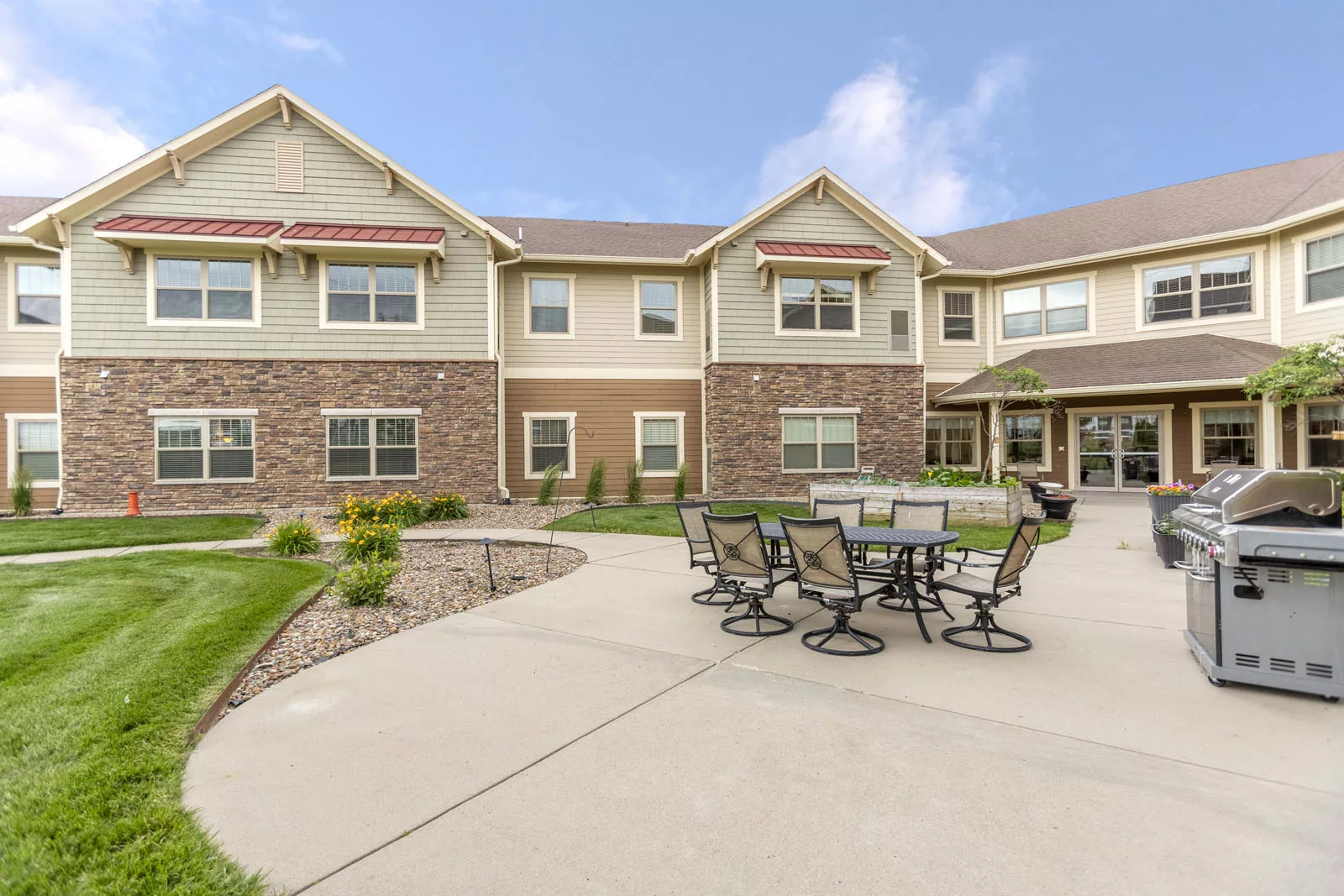 A modern residential building with an outdoor patio area featuring chairs and tables.