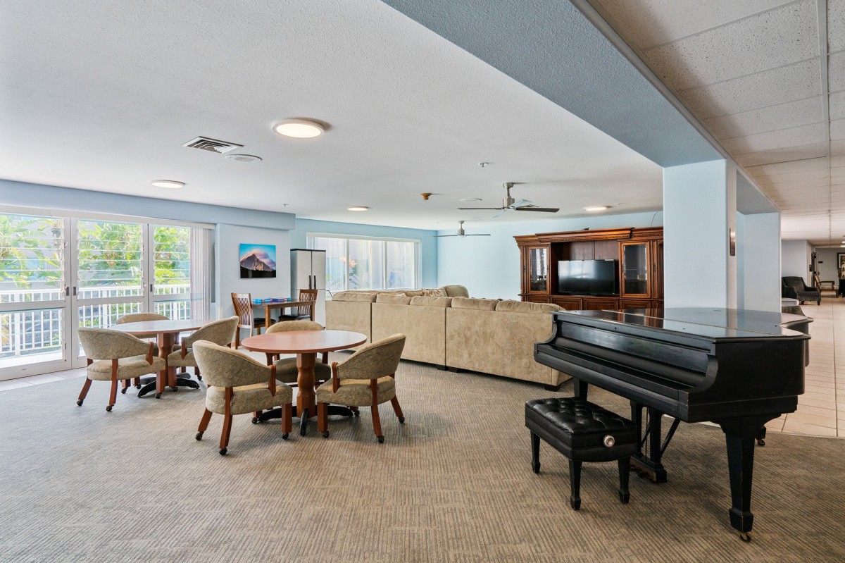A spacious living room featuring a piano, large sofa, television, and a round table with chairs.
