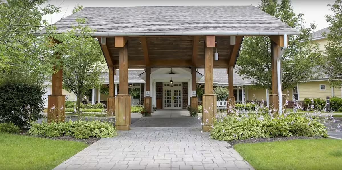 A covered entrance to a building featuring wooden pillars and landscaped surroundings.