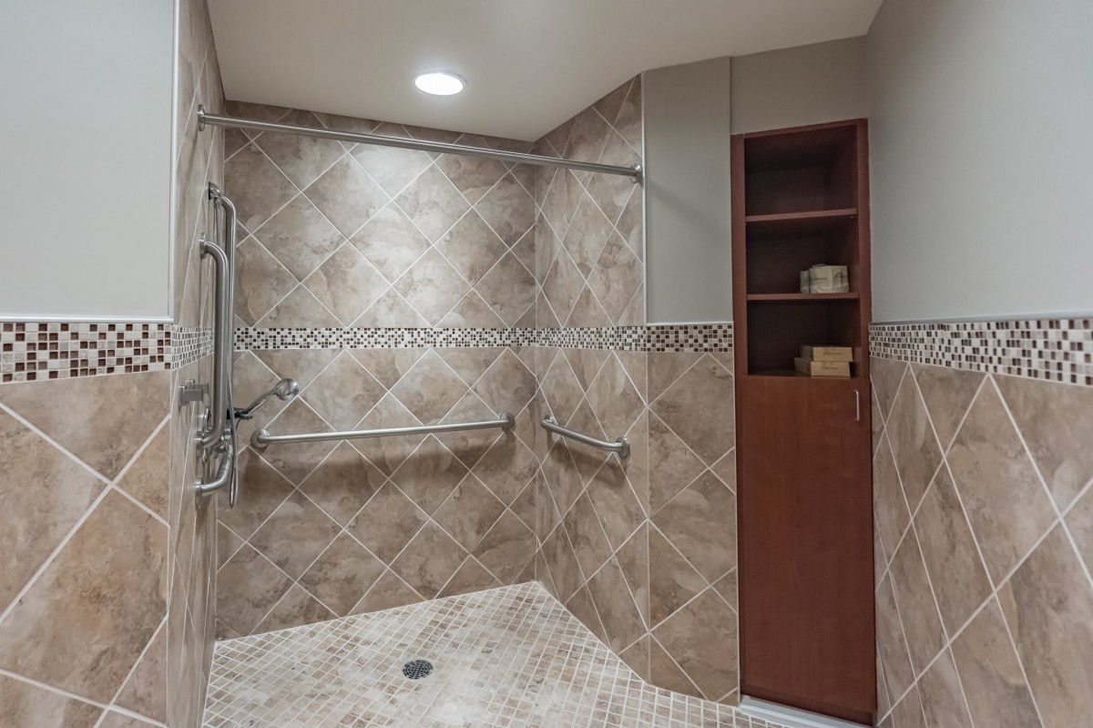 A modern, accessible bathroom with a walk-in shower featuring grab bars and tiled walls.