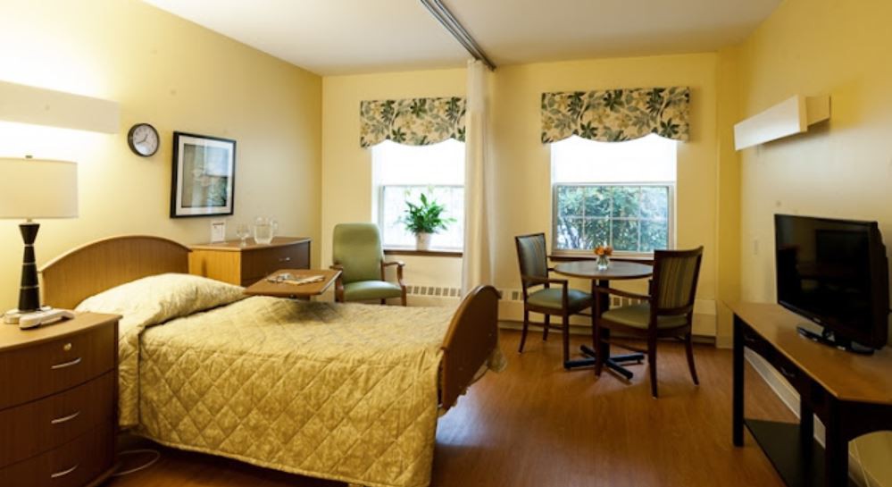A cozy bedroom with a bed, seating area, and table by the window.