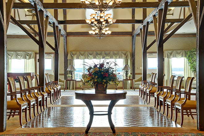 A beautifully decorated interior with wooden beams and chandeliers, featuring a central floral arrangement on a polished table.