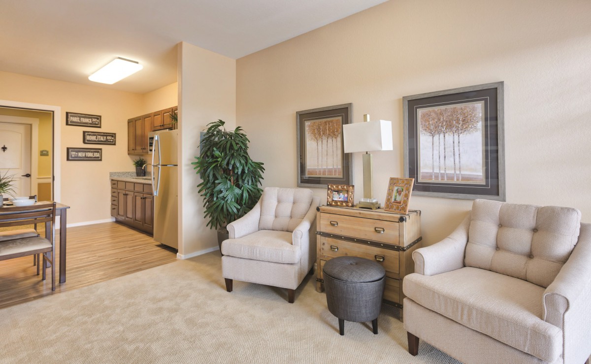 A cozy living room featuring two upholstered chairs, a wooden side table with a lamp, and decorative artwork on the walls.