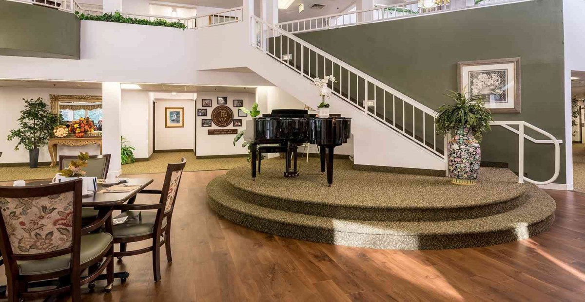 A spacious living room featuring a grand piano on a raised platform, with a staircase and artwork adorning the walls.