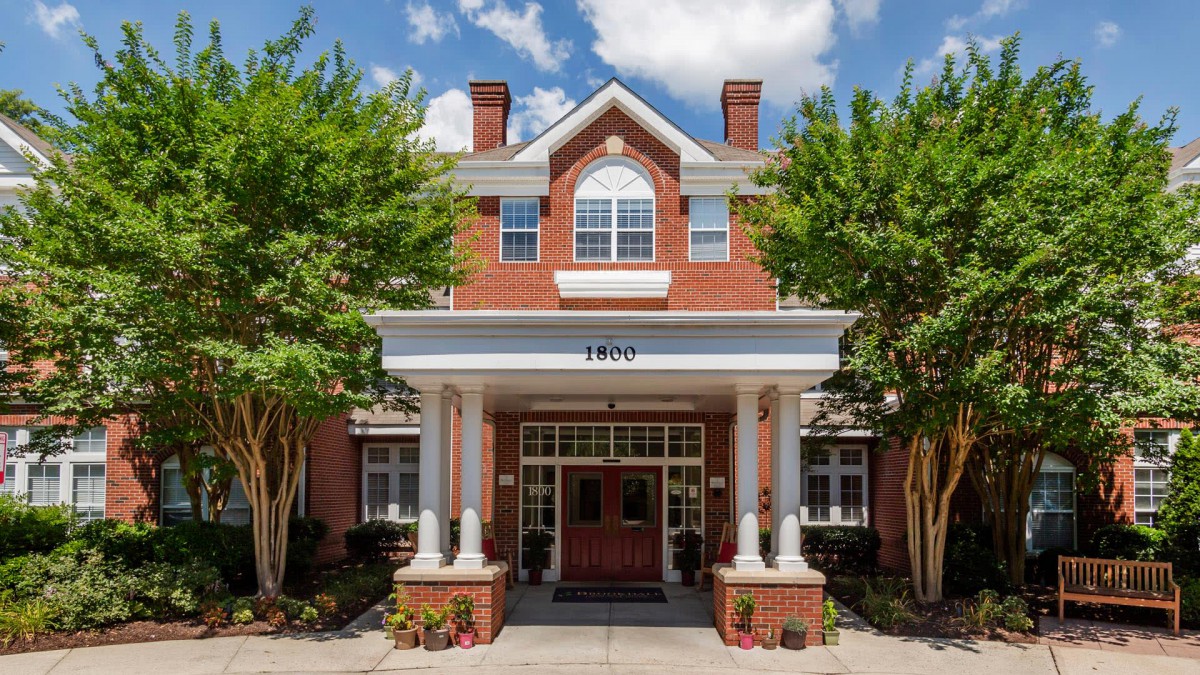 A brick building with an inviting entrance, framed by white columns and surrounded by trees.