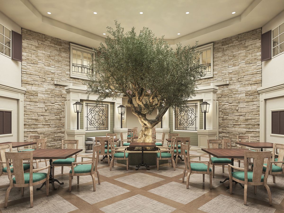 An indoor dining area featuring a large tree surrounded by tables and chairs, with stone walls adding to the ambiance.