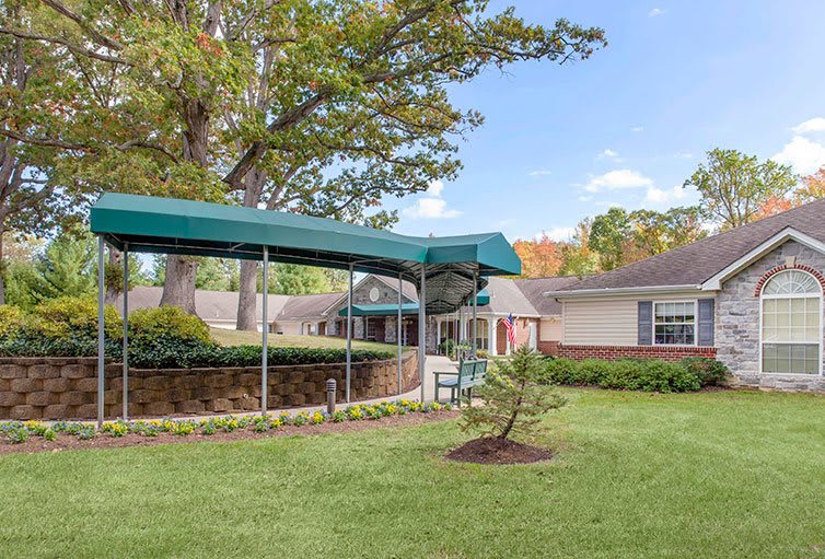 A building with a green awning surrounded by a well-maintained lawn and trees.