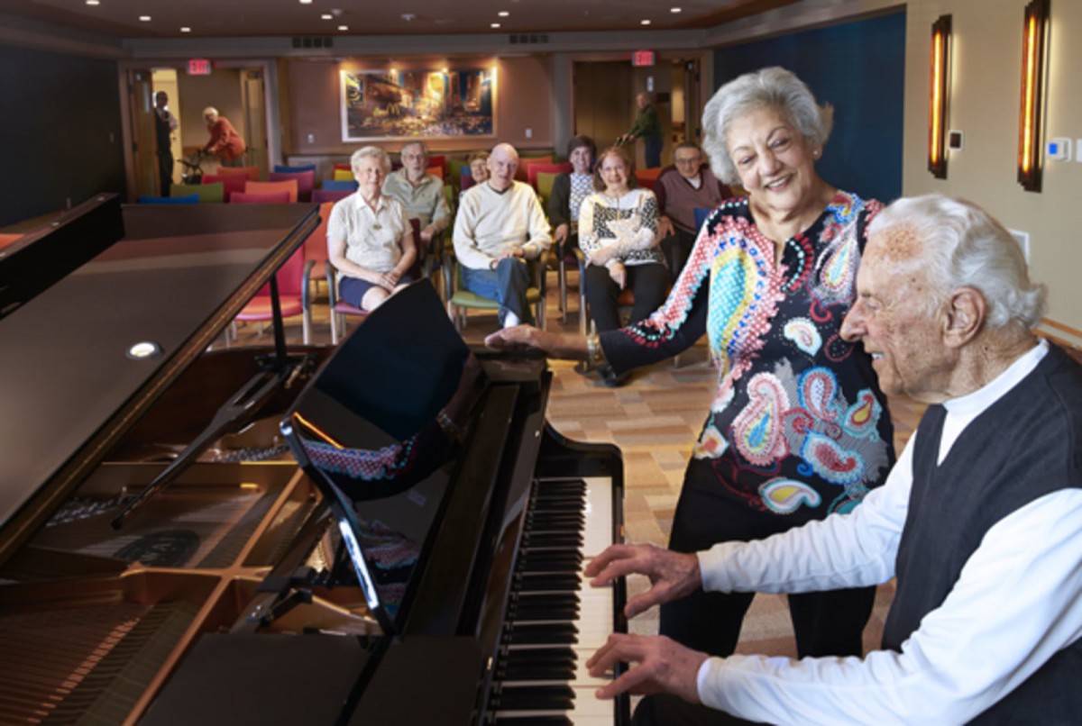 A group of senior citizens enjoying a live piano performance in a cozy indoor setting.