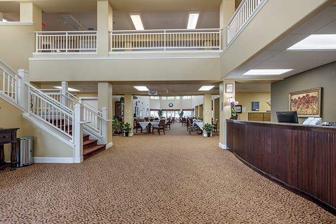A spacious lobby with carpeted flooring, a reception desk, and an open area leading to a seating arrangement.