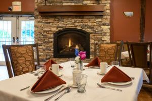A cozy dining setup in front of a fireplace, complete with neatly arranged napkins and tableware.