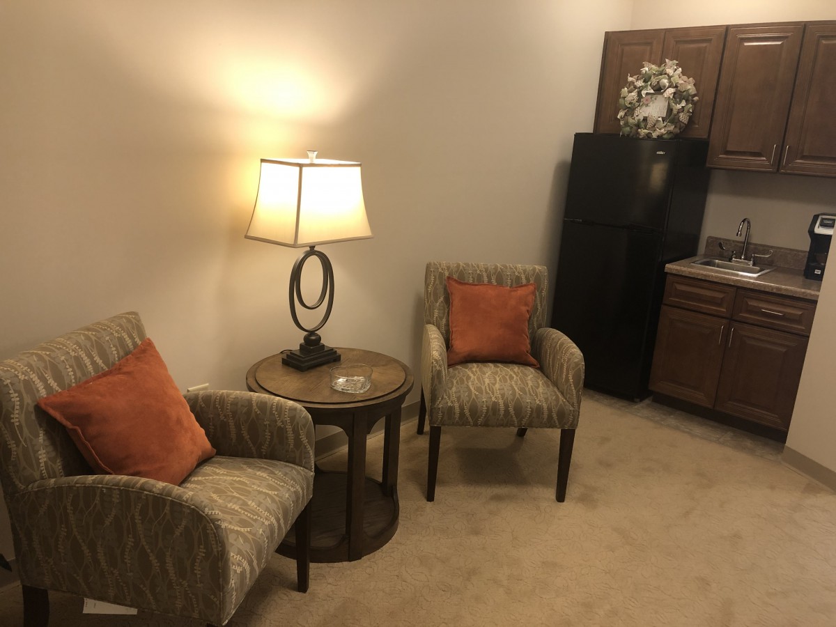 A cozy corner of a living room with two chairs, a lamp, and a small kitchenette.