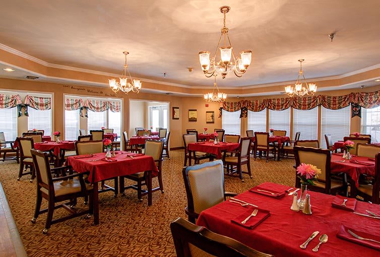 A formal dining room with red tablecloths and elegant chandeliers.