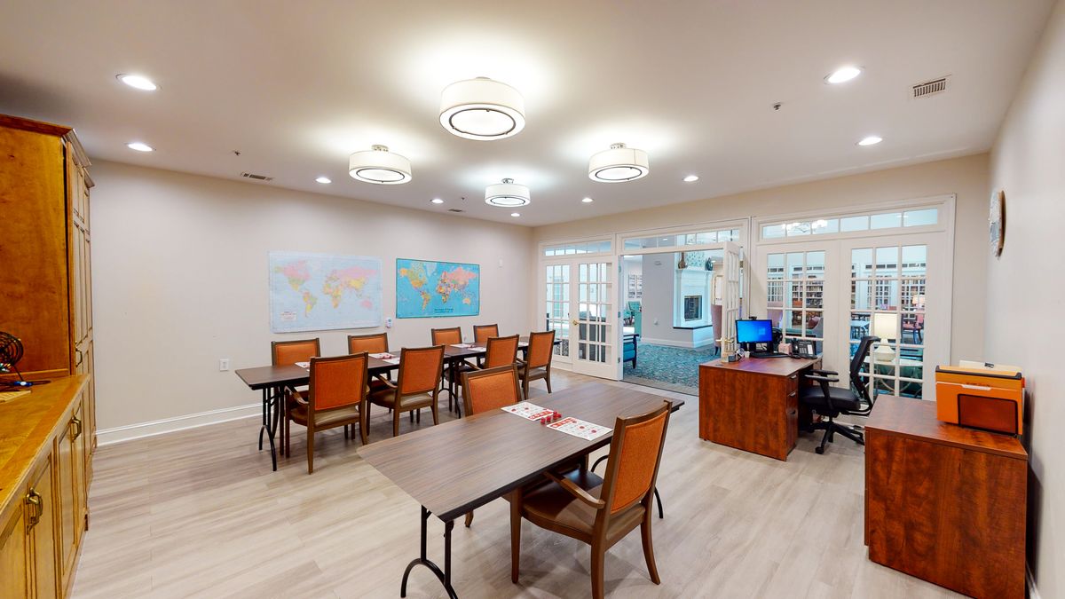 A modern meeting room with multiple tables and chairs, featuring maps on the wall and bright overhead lighting.