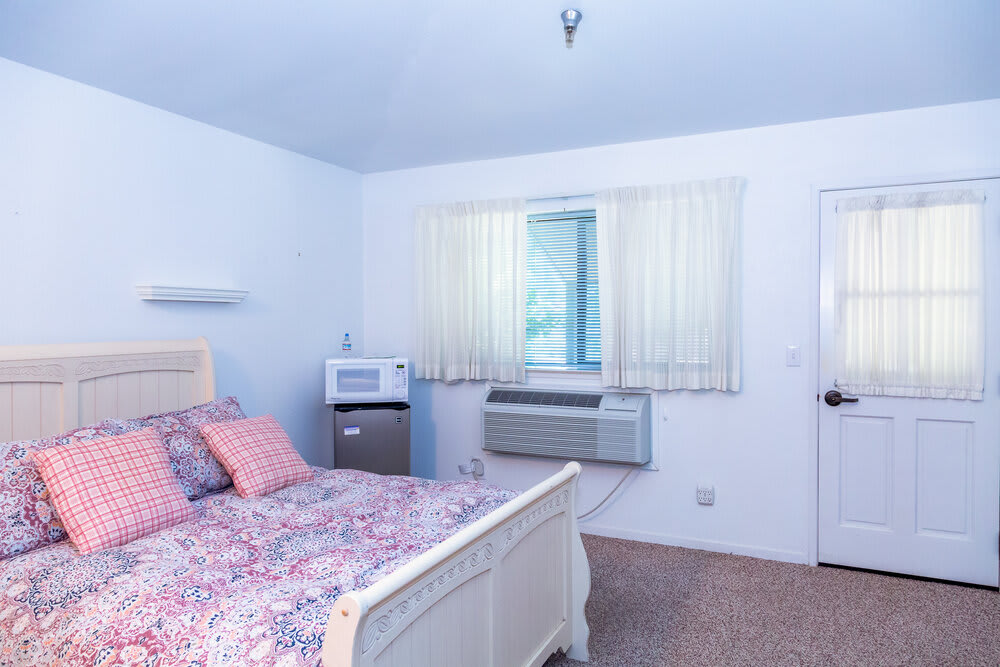 A cozy bedroom with a bed, air conditioner, microwave, and mini fridge.