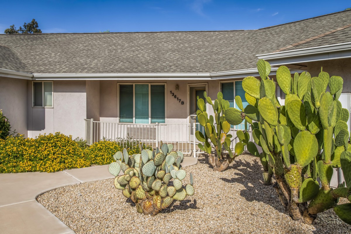 A cozy house with desert landscaping featuring cacti in the front yard on a sunny day.