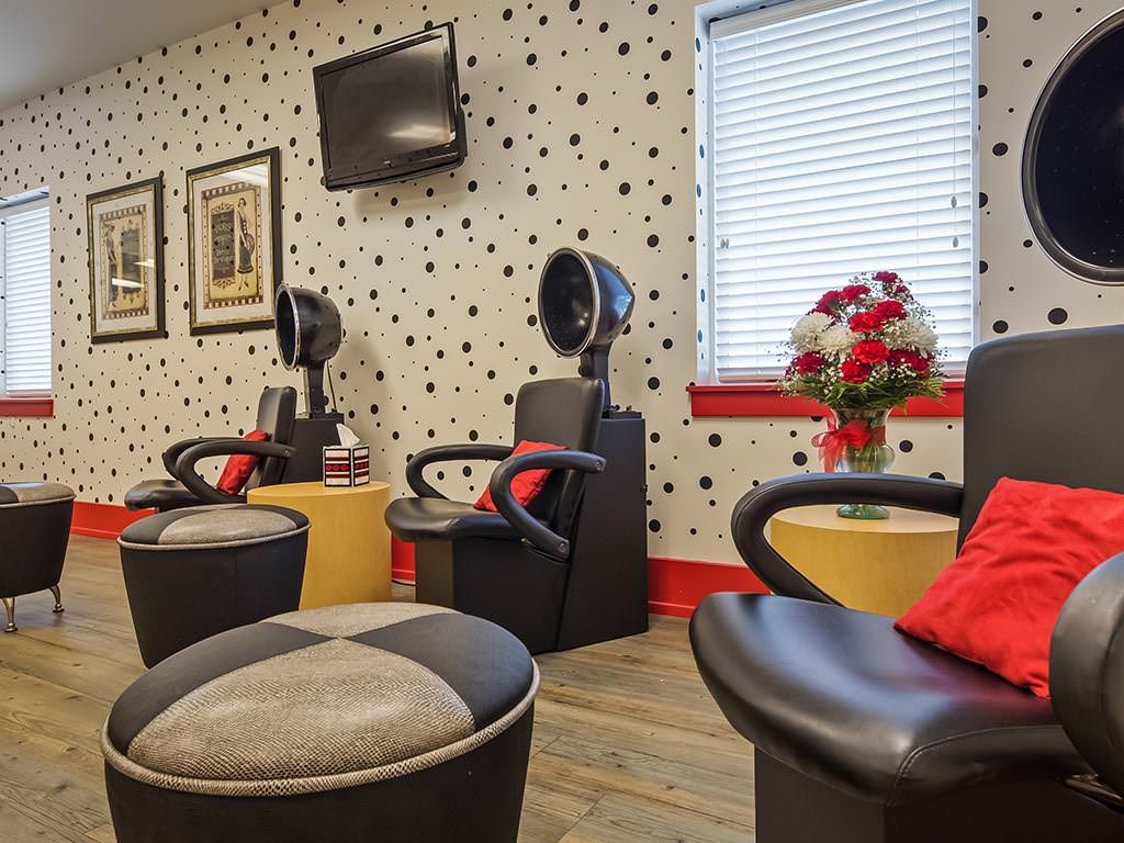 A modern salon interior with styling chairs and hair dryers against polka dot wallpaper.