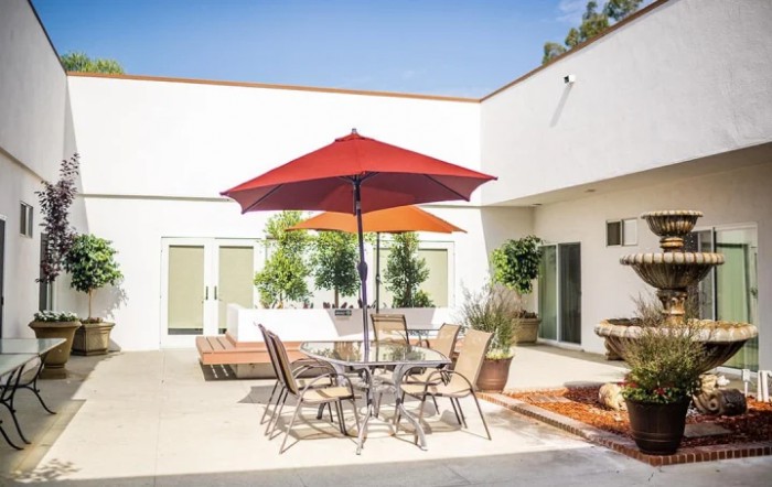 A sunny courtyard with a patio table and chairs set under a red umbrella.