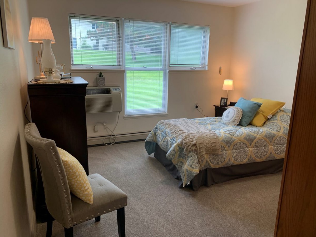A cozy bedroom with a large window, bed, and soft lighting.