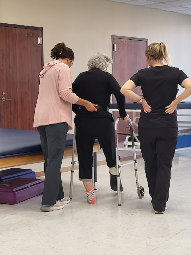 Healthcare professionals assisting an older adult with walking using a walker.