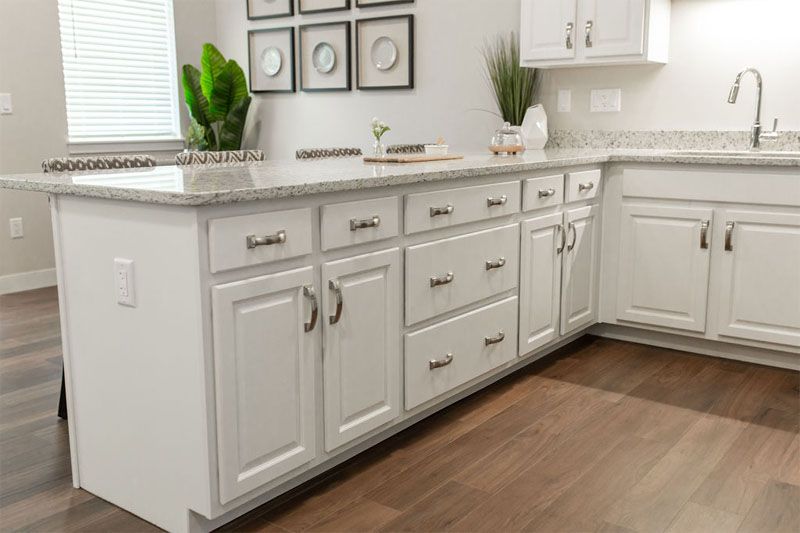 A modern kitchen with white cabinets and a marble countertop, adorned with decorative plants.