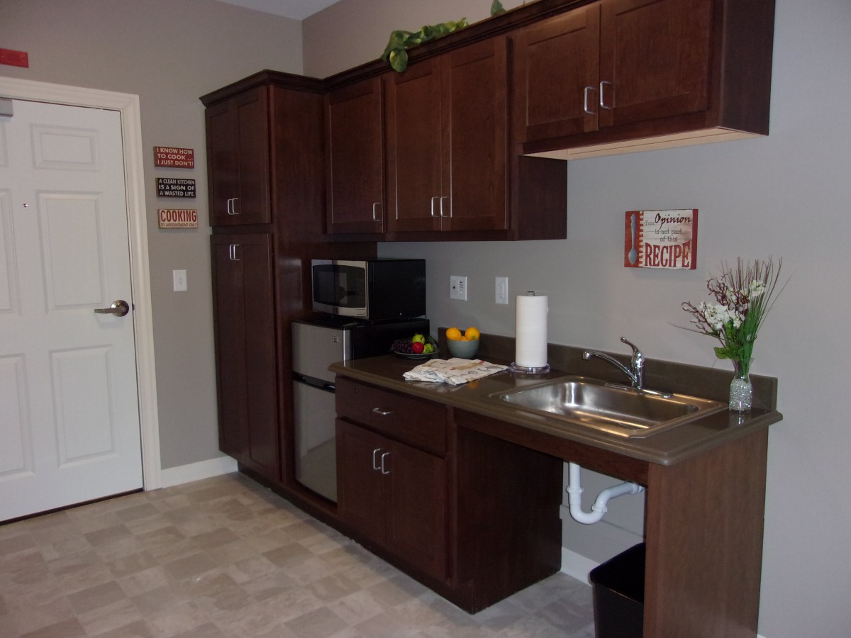 A compact kitchen area featuring dark wood cabinets, a microwave, and a small sink.