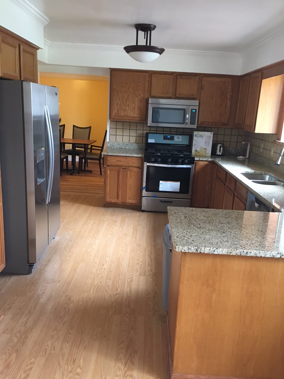 A modern kitchen with wood cabinets and granite countertops, featuring stainless steel appliances and a view into the dining room.