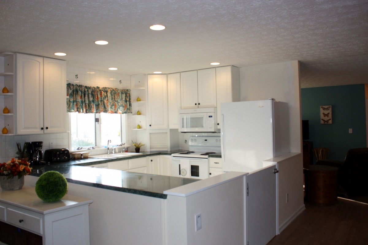 A modern kitchen with white cabinetry, appliances, and bright lighting.
