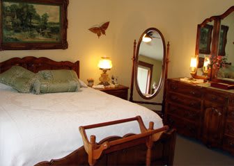 A cozy bedroom with wooden furniture, including a bed, dresser, and an oval mirror.